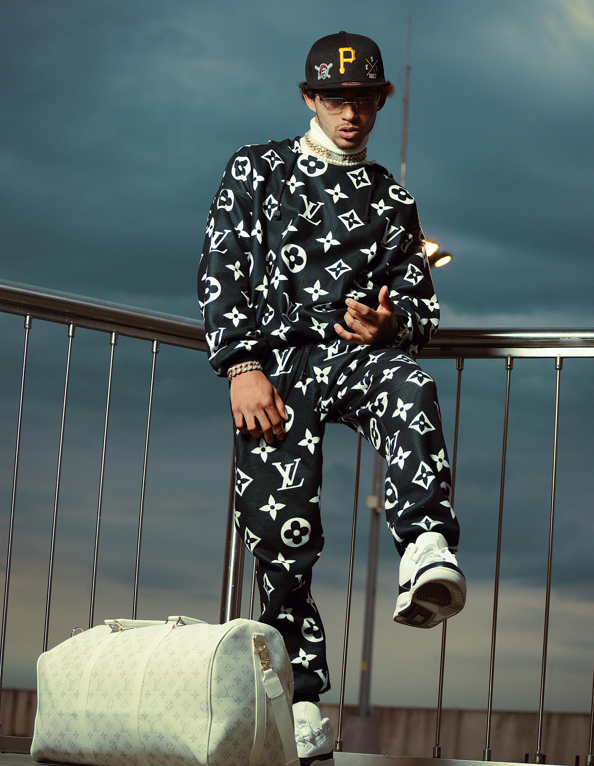 Fashionable man in designer wear with branded bag, standing outdoors on a railing.